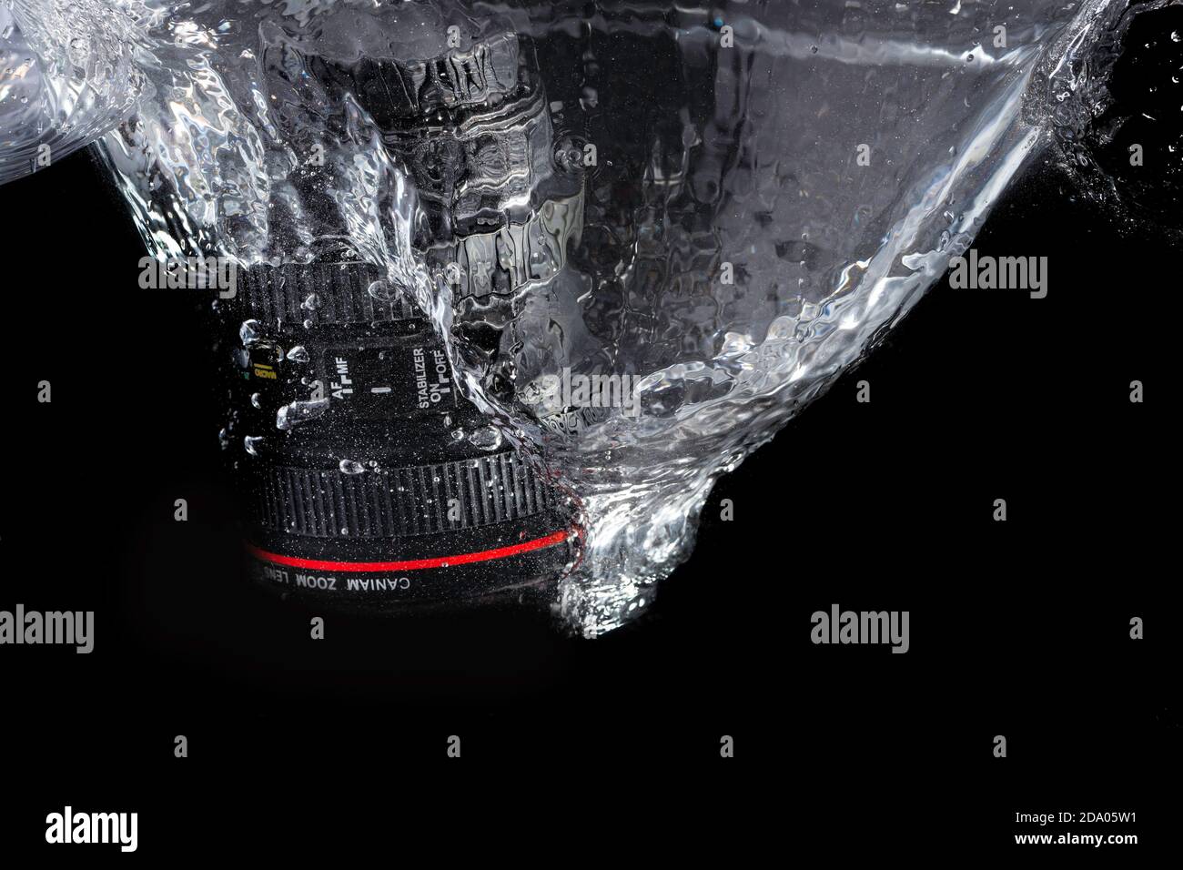 DSLR camera lens splashing into  water on a black background Stock Photo