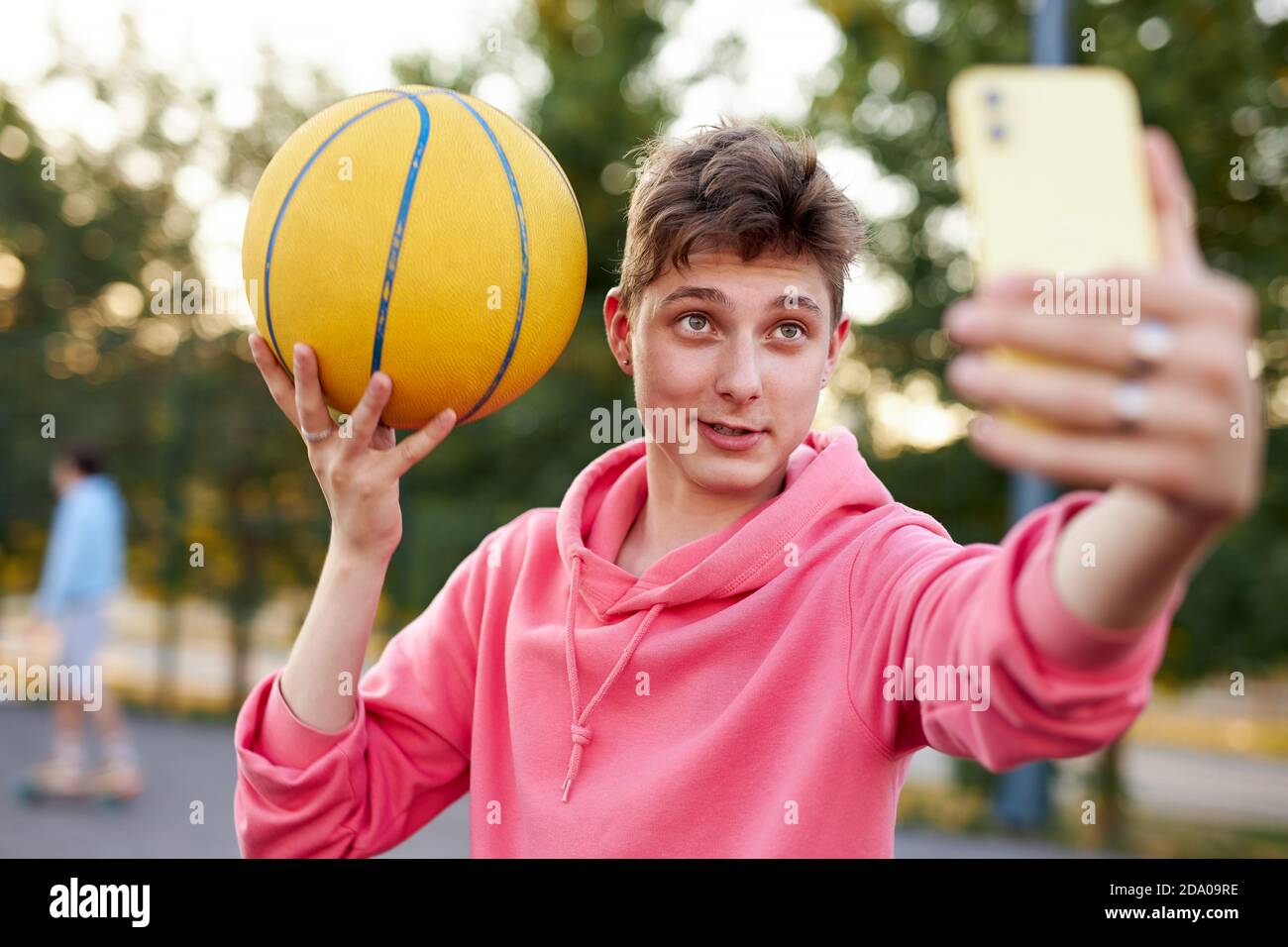 handsome caucasian teen boy take selfie on smartphone holding basketball ball, take photo. at sport playground Stock Photo