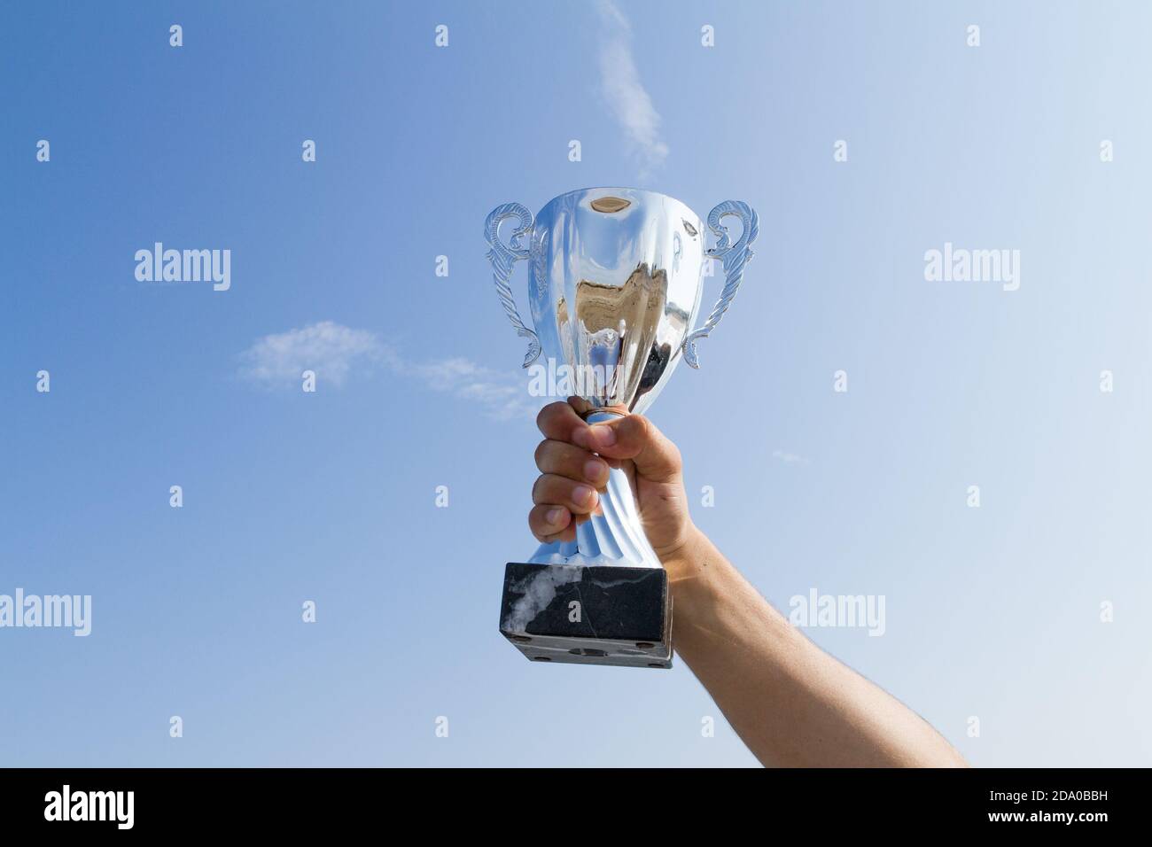 Male athlete holding up a trophy cup. Competition winner athlete displaying champion trophy cup on blue sky background. Sports, achievement, success c Stock Photo