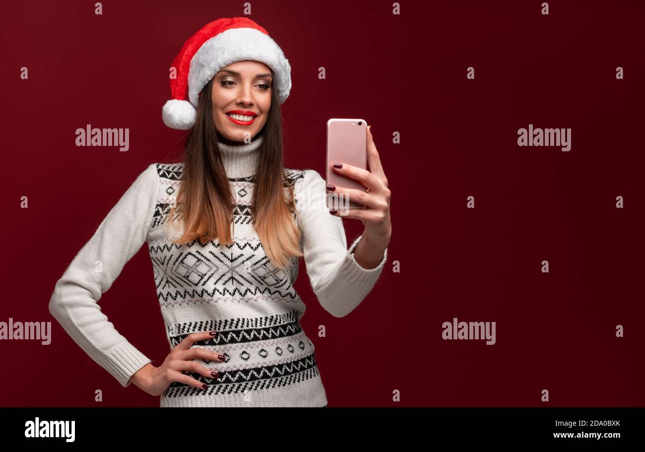 Close up portrait beautifiul caucasian woman in red Santa hat on red studio background. Christmas New Year holiday concept. Cute girl teeth smiling po Stock Photo
