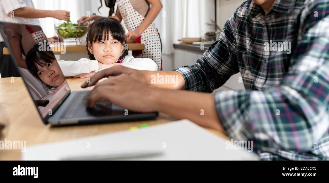 Panoramic Asian upset girl waiting her father working from home while city lockdown in dining room while mom and grandfather cooking in kitchen. Domes Stock Photo