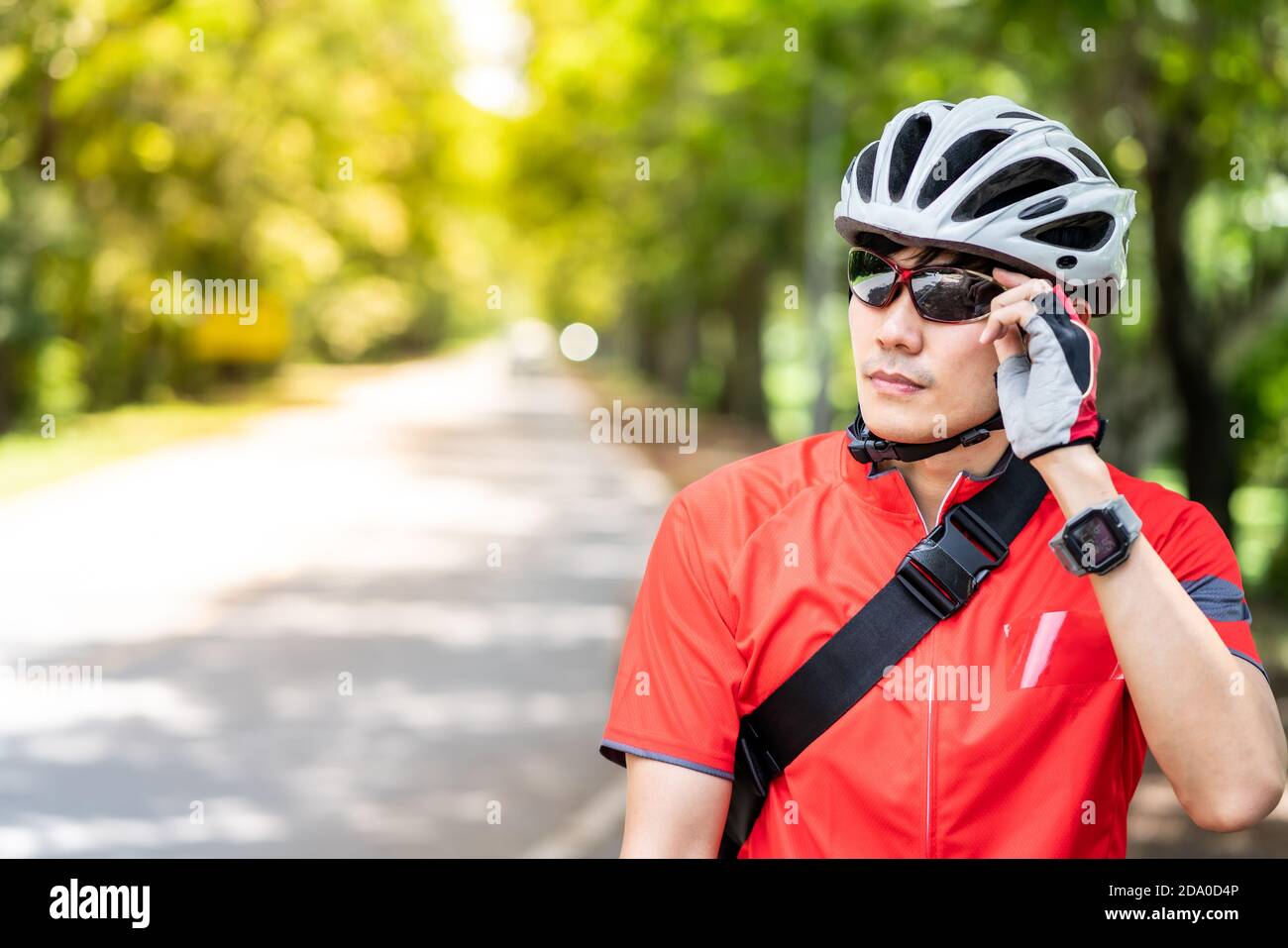 Portrait of asian male cyclist in sportsware shirt with his bicycle in countryside road with green tree in background. Weekend outdoor sport athlete a Stock Photo