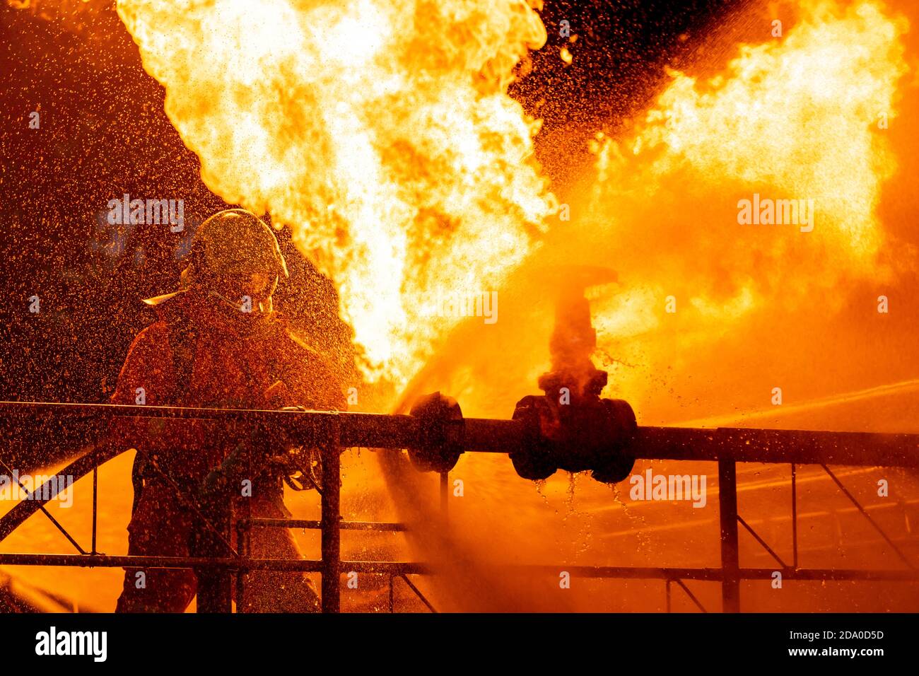 Firefighter using water fog type fire extinguisher to fighting with the fire flame from oil pipeline leak and explosion on oil rig and natural gas sta Stock Photo