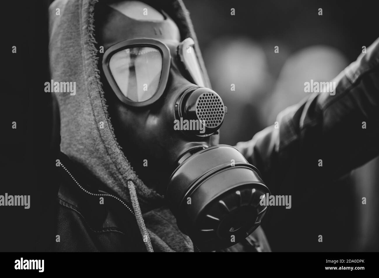 Shallow depth of field (selective focus) image with a protestor wearing a hoodie and a military gas mask. Stock Photo