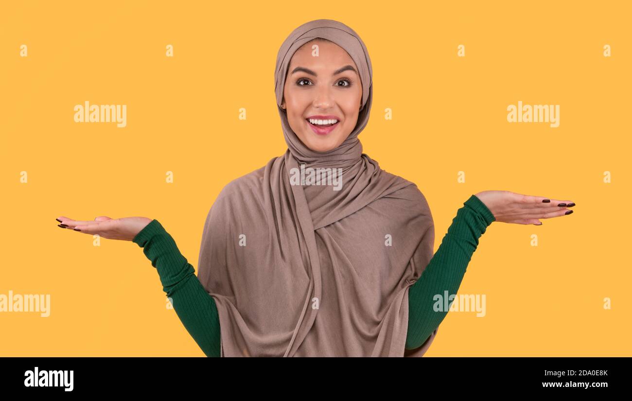 Muslim Lady In Hijab Shrugging Shoulders Standing Over Yellow Background Stock Photo