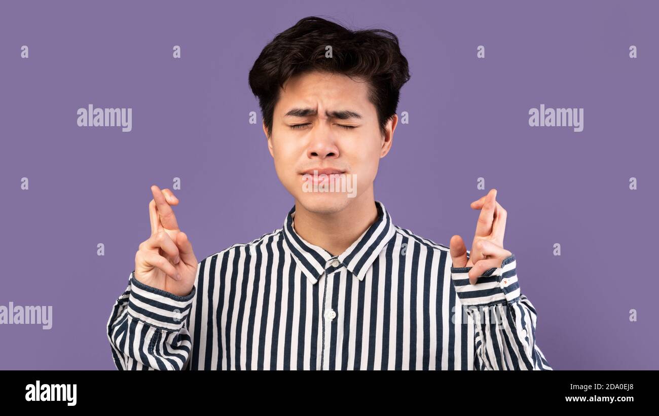 Hopeful young asian guy crossing his fingers Stock Photo