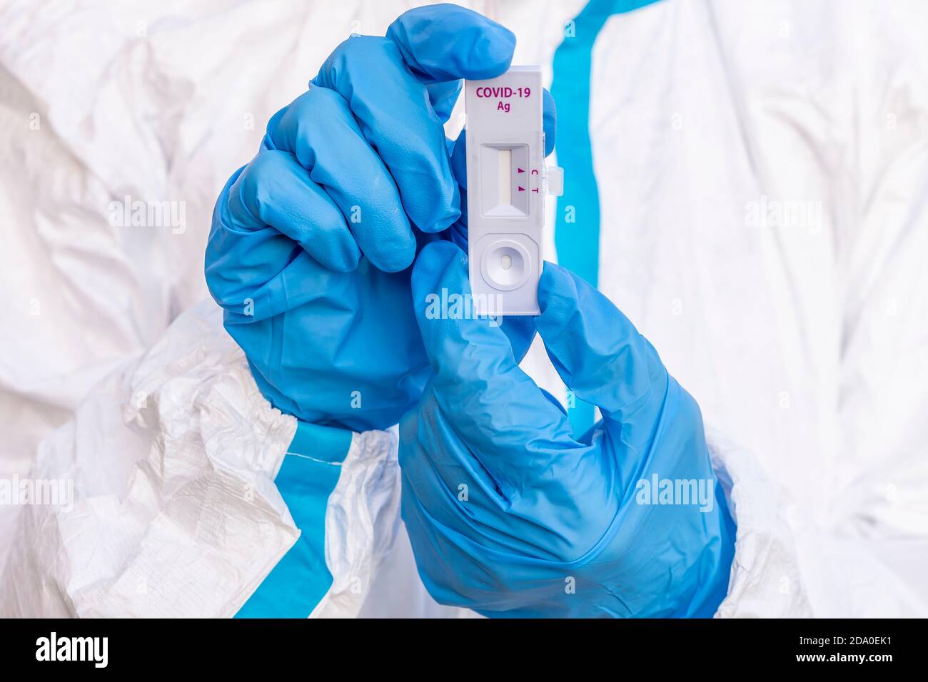 A healthcare worker covered by a white coverall and with blue gloves shows a rapid test for the control of a possible contagion from covid-19 Stock Photo