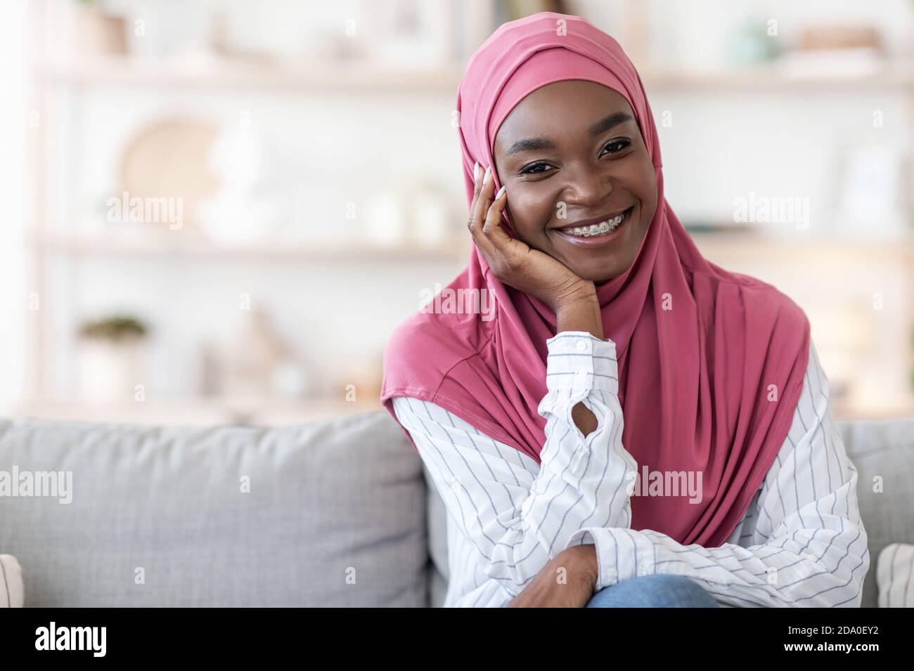 Modern Modesty. Smiling black woman in hijab posing on sofa at home ...