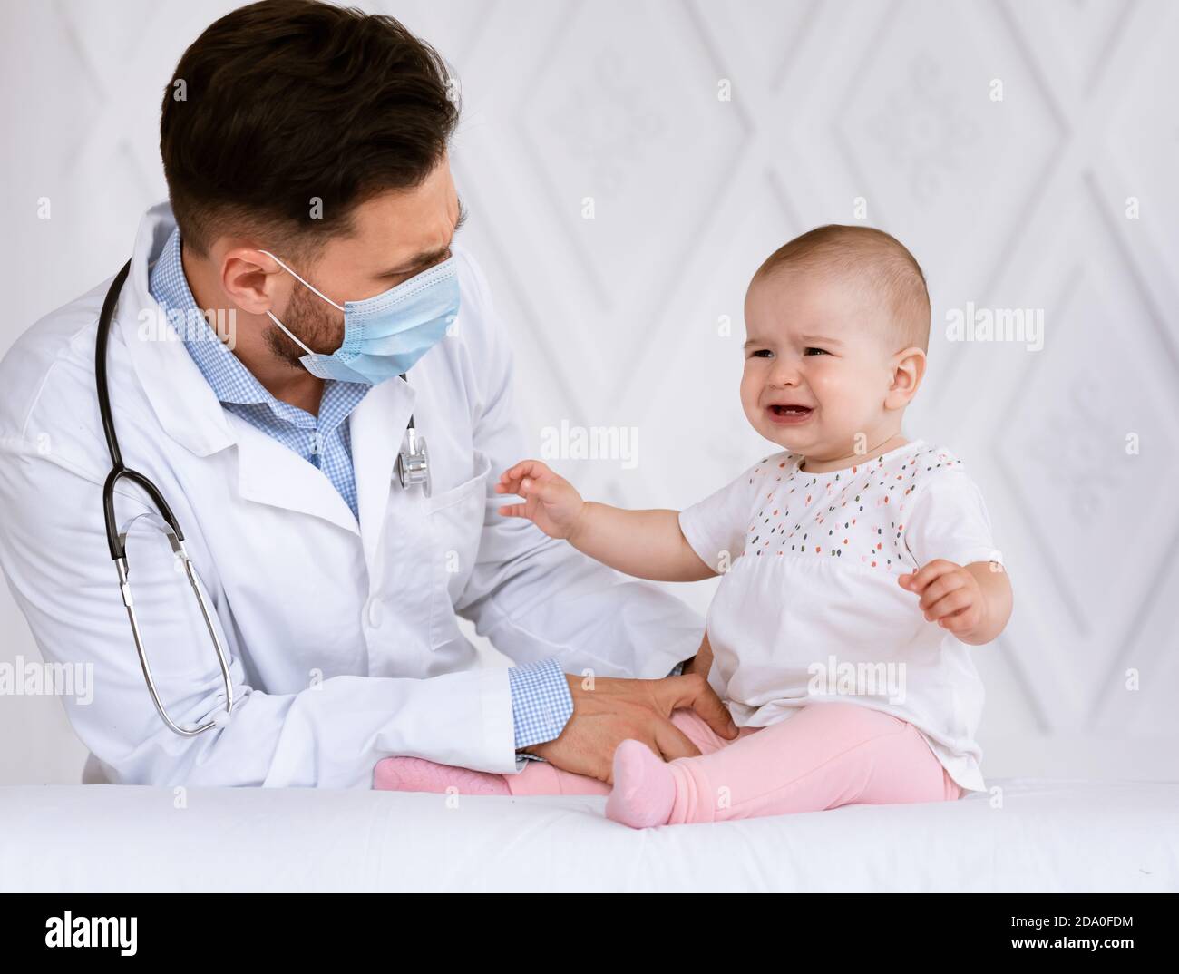 Doctor In Face Mask Examining Little Baby Girl In Clinic Stock Photo