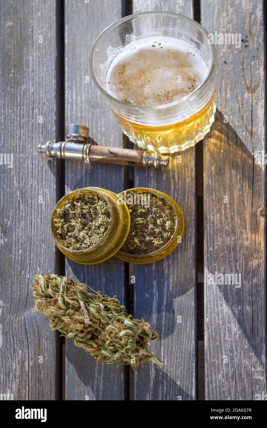 High angle view of table with marijuana grinder, marijuana bud, a smoking pipe and glass of beer in the background. Stock Photo