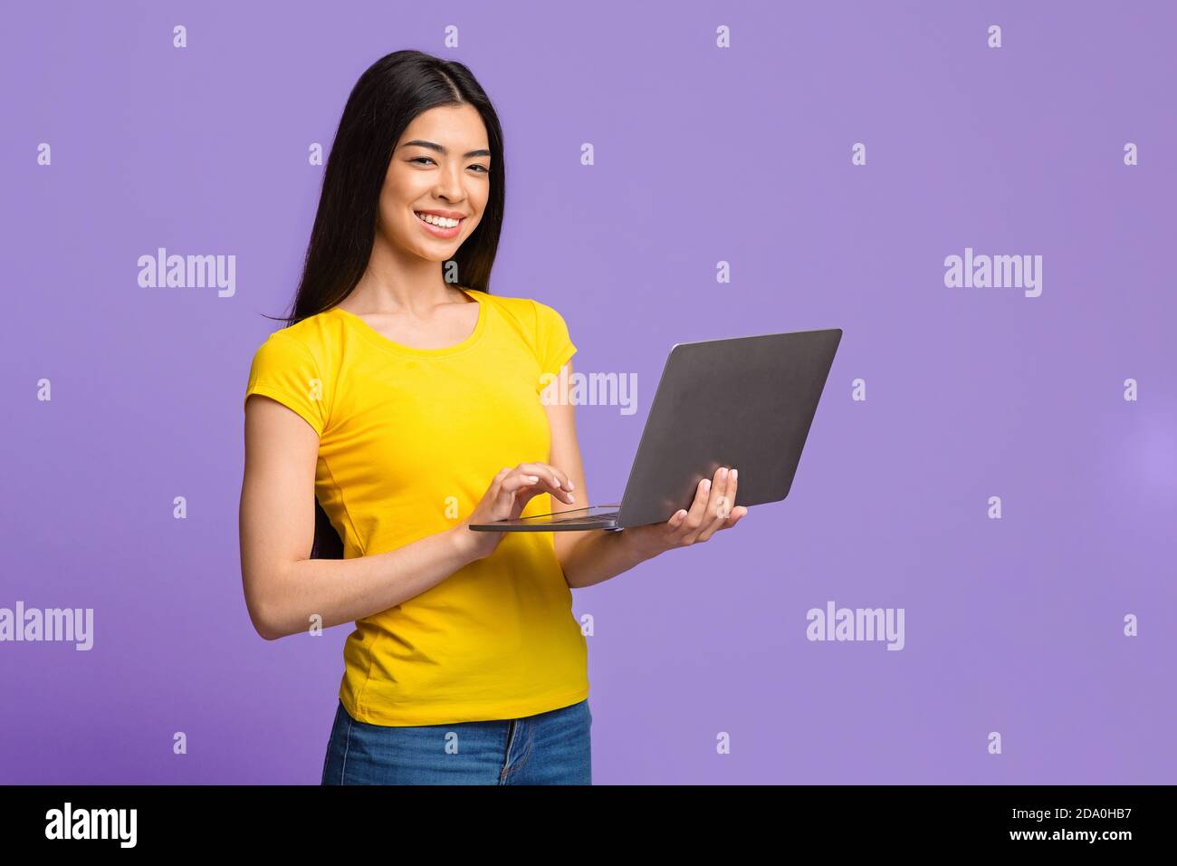 Positive Young Asian Woman Posing With Laptop Computer Over Purple Background Stock Photo