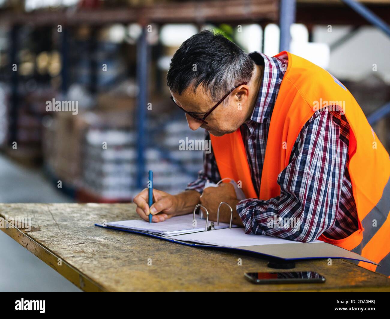 Side view adult worker wearing uniform writing on clipboard while working in spacious storehouse Stock Photo