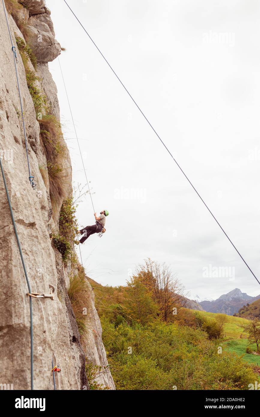 Strong male alpinist in safety equipment climbing on rocky cliff on