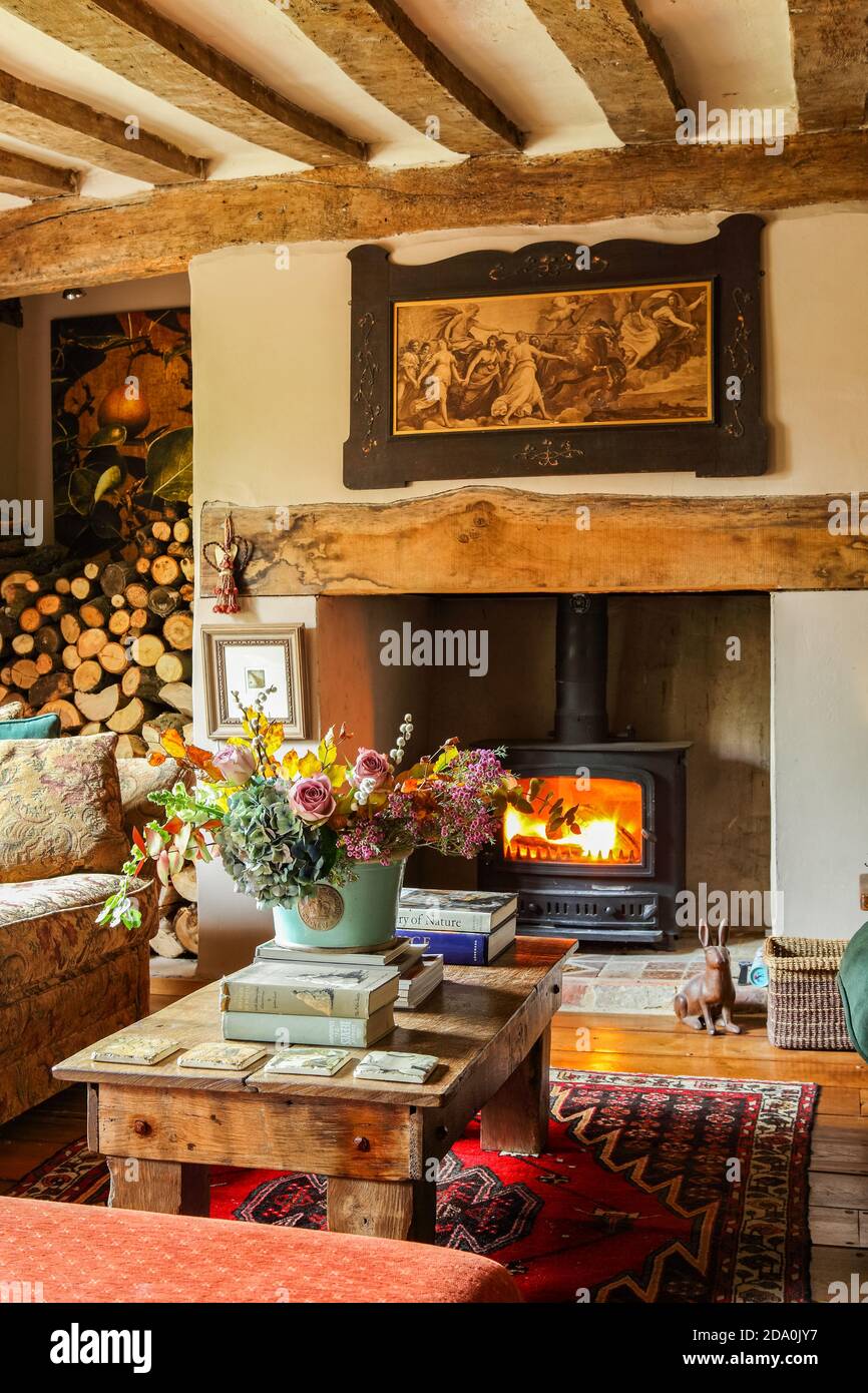 Interior of an English cottage with lit wood burner and floral display in a  confortable lounge with exposed ceiling timbers Stock Photo - Alamy