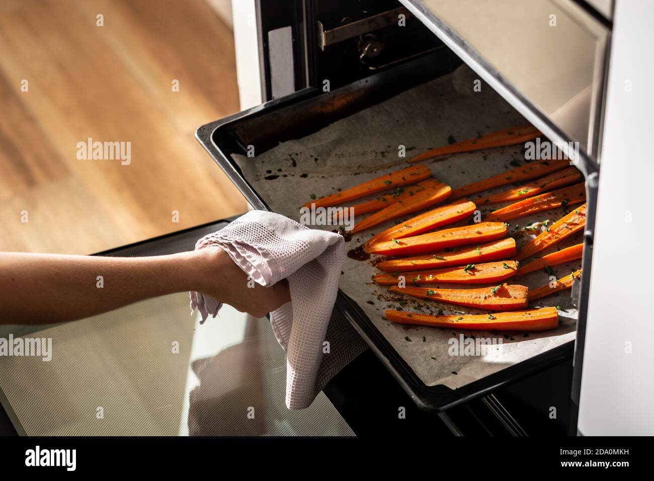 Cropped unrecognizable person getting tray with honey glazed carrots out of oven Stock Photo