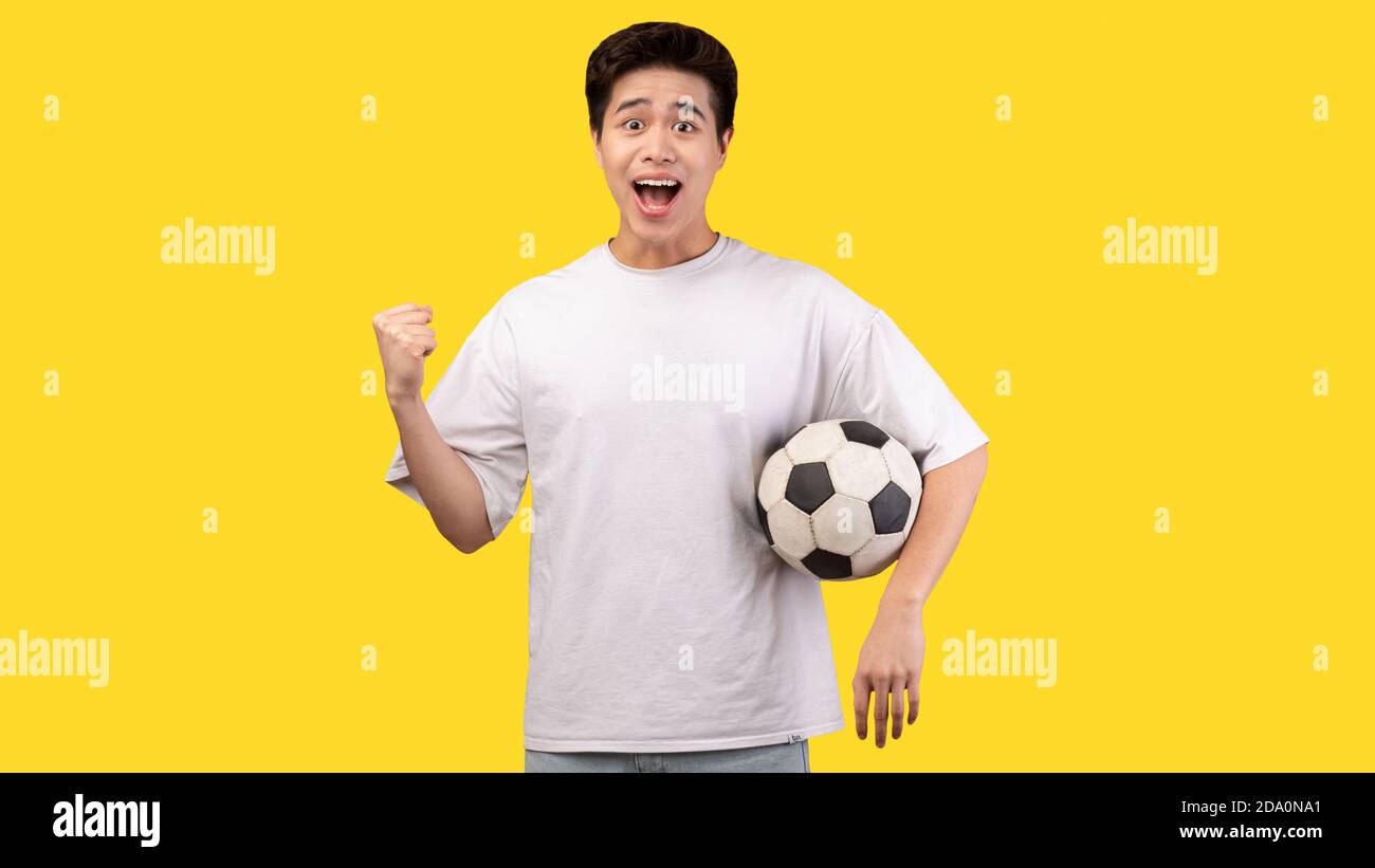 Asian man posing with soccer ball on yellow background Stock Photo