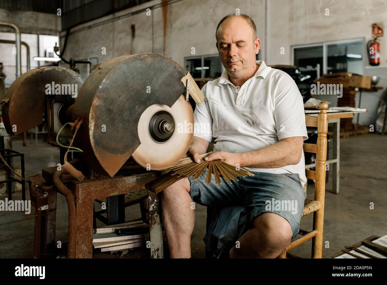 Craftsman using grinding machine while making creative wooden folding fan in shabby workshop Stock Photo
