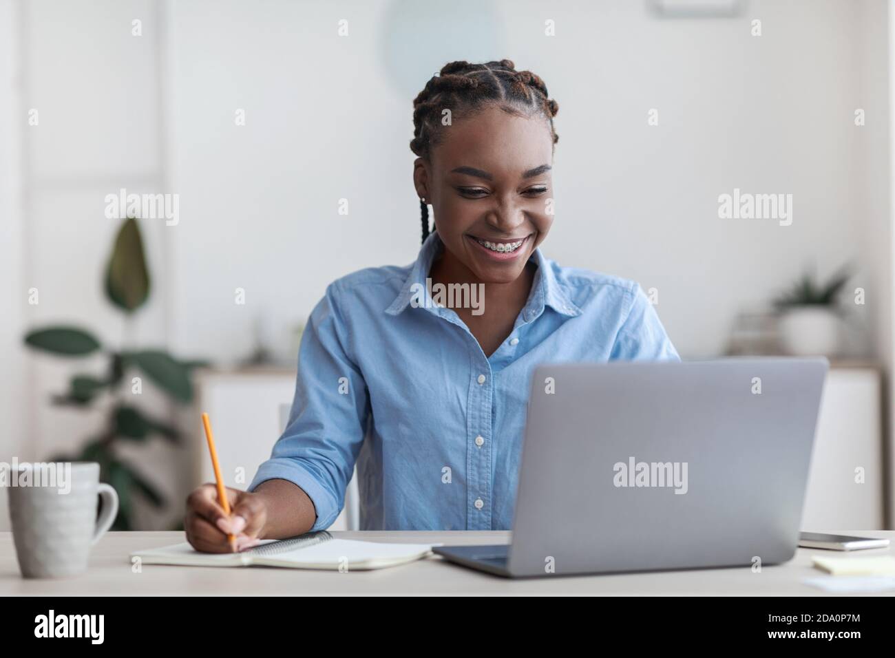Online Education. Young Black Female Student Using Laptop At Home, Taking Notes Stock Photo