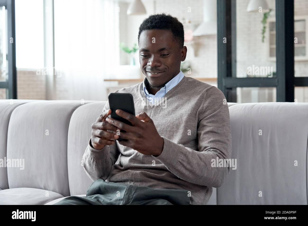 African american man using mobile apps sitting on couch at home. Stock Photo