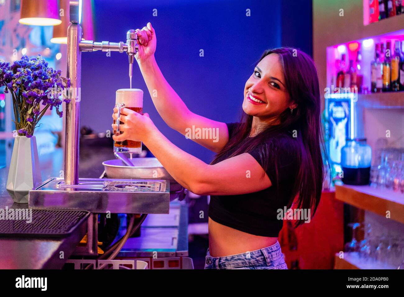 Side view of female bartender pouring alcoholic drink into glass while