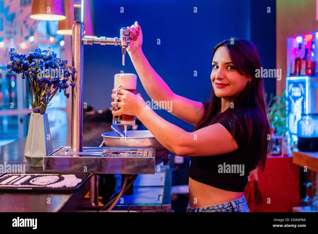 Side view of female bartender pouring alcoholic drink into glass while