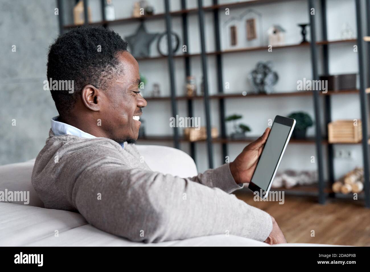Happy african man using digital tablet apps sitting on couch at home. Stock Photo