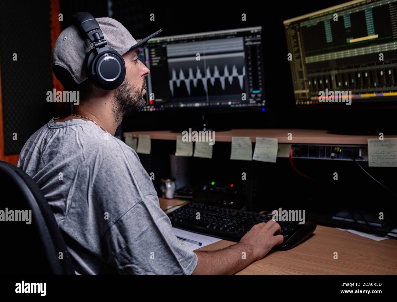 Side view of male musician sitting at table with monitors and stereo speakers while recording audio in studio Stock Photo