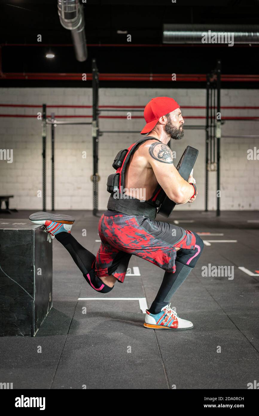 Side view of muscular sportsman in weight vest and with heavy disc doing  squats during workout in gym Stock Photo - Alamy
