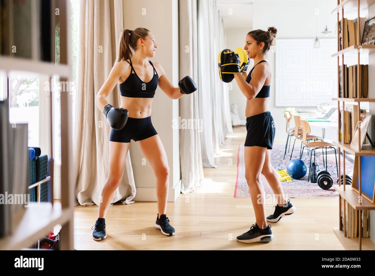 Side view of fit female fighter in gloves and personal coach in boxing mitts  standing in living room and preparing for workout Stock Photo - Alamy