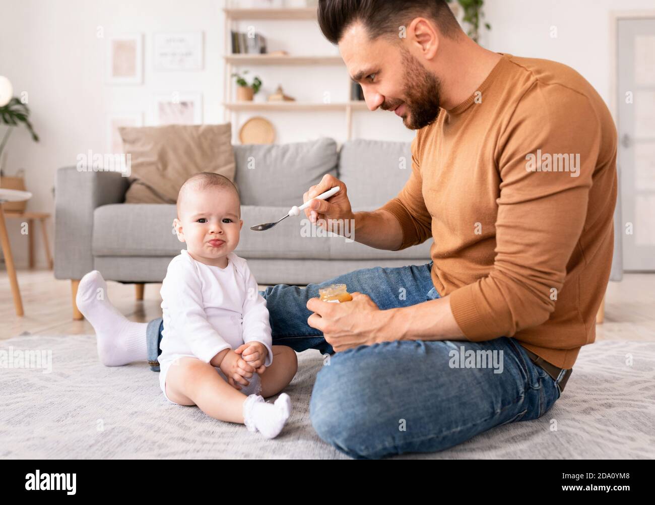 Dad Spoon Feeding Baby During Paternity Leave At Home Stock Photo