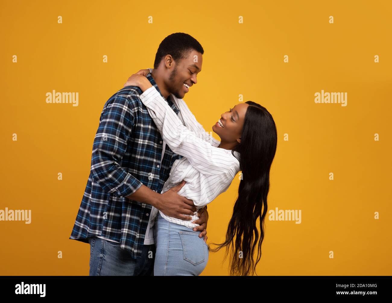 Smiling young african american man and lady have fun, hug and look at ...