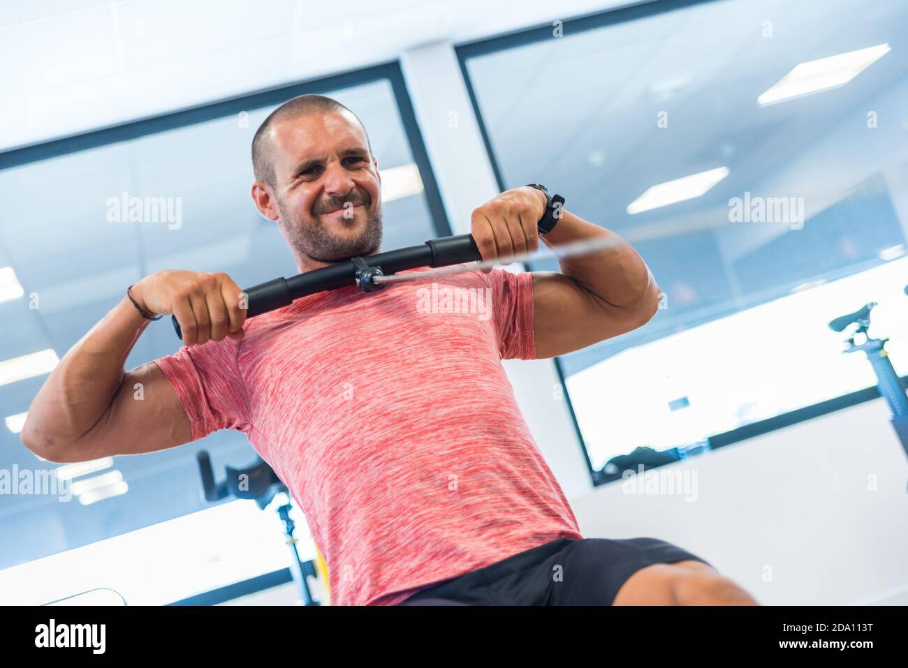 Concentrated athletic male doing exercises on rowing machine while ...