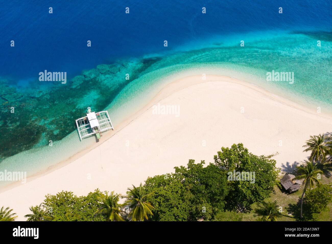 Tropical beach of white sand, top view. Tourist boat off the coast. Blue sea with turquoise lagoons. Tranquil beach scene. Stock Photo