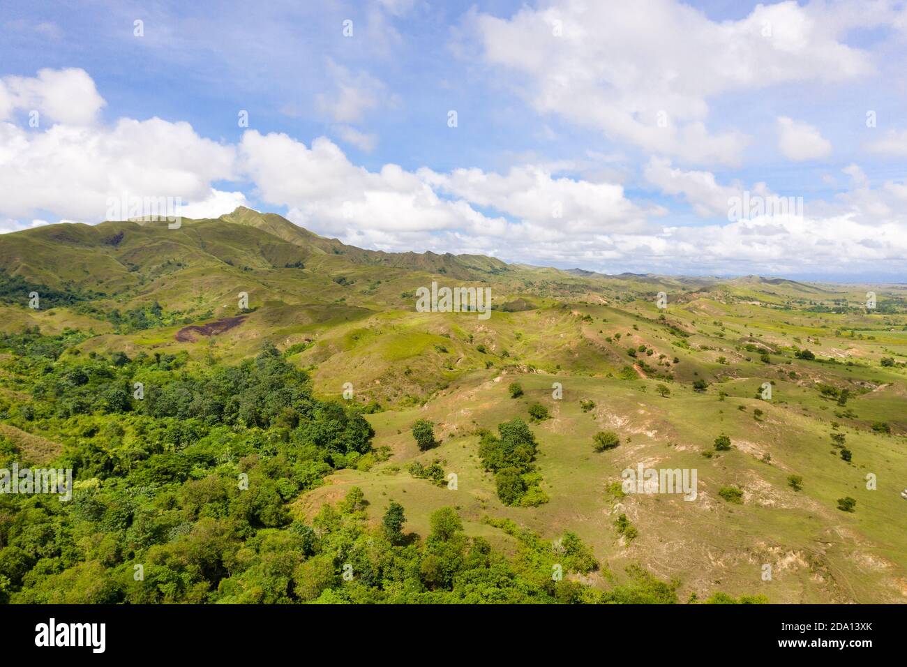 Hills with green grass and blue sky with white puffy clouds. Beautiful landscape on the island of Luzon, aerial view. Stock Photo