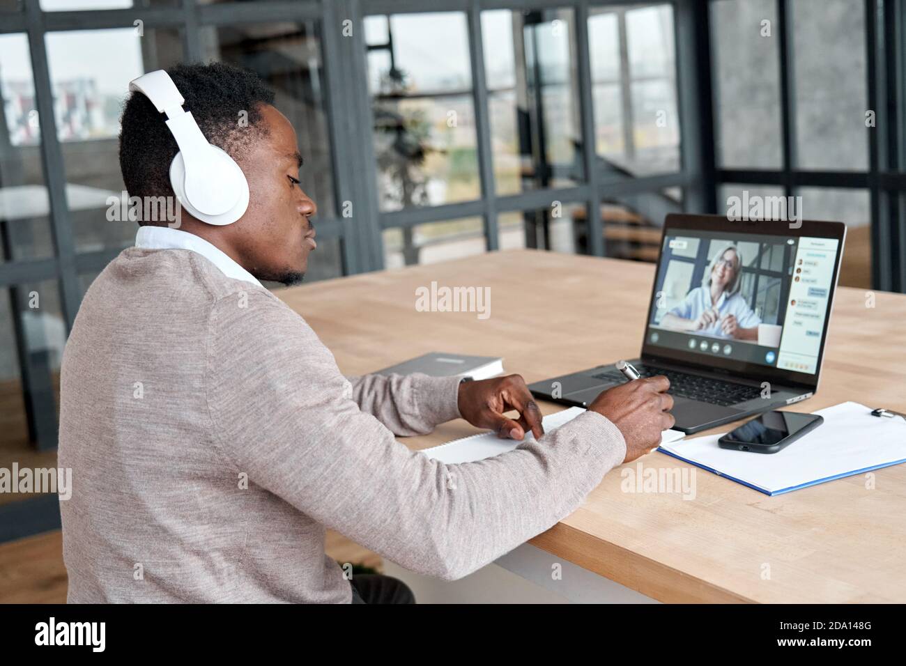 African business man wearing headphones video calling watching webinar. Stock Photo