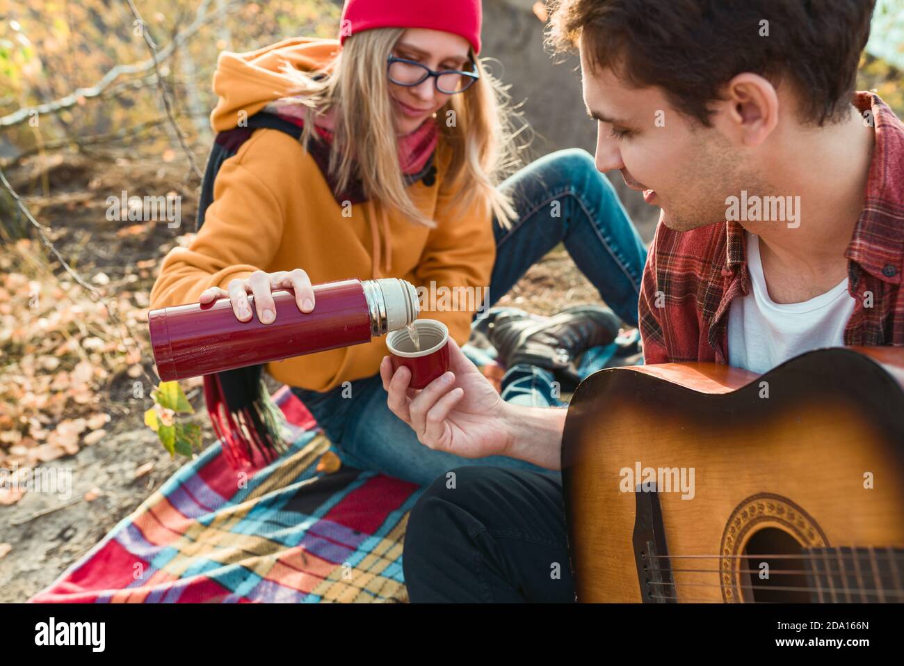 A couple are resting in nature, against the background of autumn trees and the river. Guy plays the guitar Stock Photo