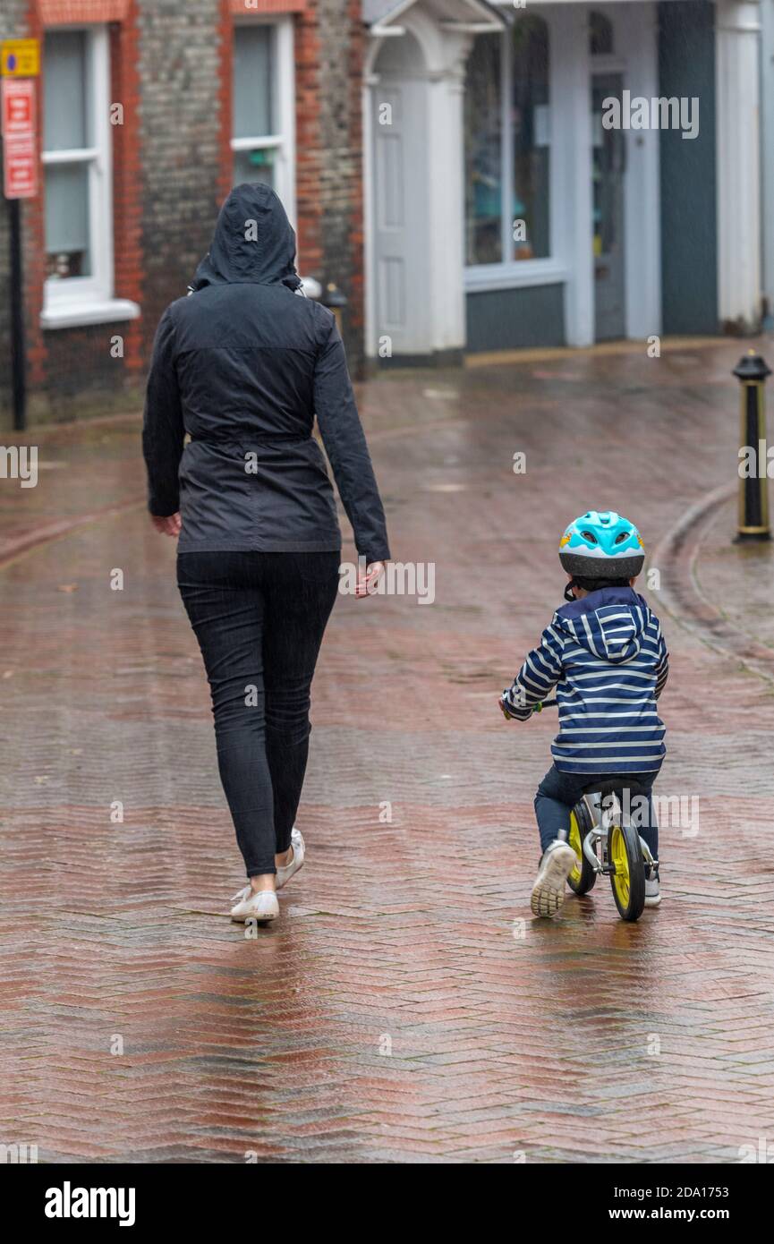 a woman or mother and small child riding a bicycle by her side walking in the rain on an autumn day. Stock Photo