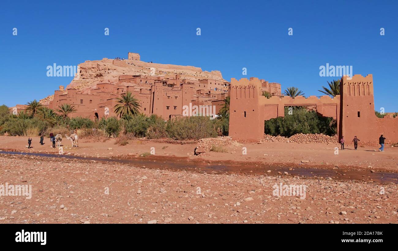 Tourists shooting pictures with a camel below historic Moorish ksar Ait Benhaddou, UNESCO World Heritage Site, with historic loam buildings. Stock Photo