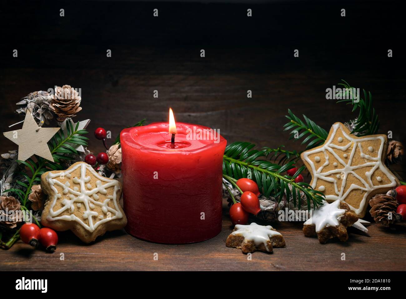 Christmas decoration with a red burning candle, gingerbread cookies, rose hips, branches and cones on a dark rustic wooden background, copy space, sel Stock Photo