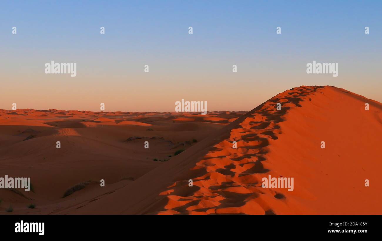 Peak of a huge orange colored sand dune in the evening light with footprints in the sand in the desert of Erg Chebbi near Merzouga, Morocco, Africa. Stock Photo