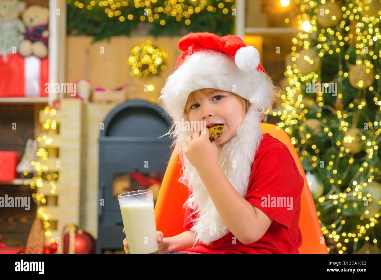 Santa boy child eating cookies and drinking milk. Santa boy in Santa hat. Stock Photo