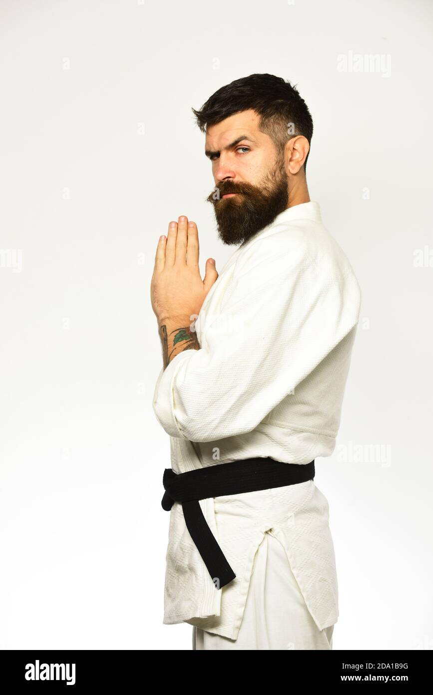 Taekwondo master with black belt holds hands together in greeting. Man with beard in white kimono on white background. Karate man with strict face in uniform. Japanese martial arts concept Stock Photo - Taekwondo master with black belt holds hands together in greeting. Man with beard in white kimono on white background. Karate man with strict face in uniform. Japanese martial arts concept Stock Photo -
