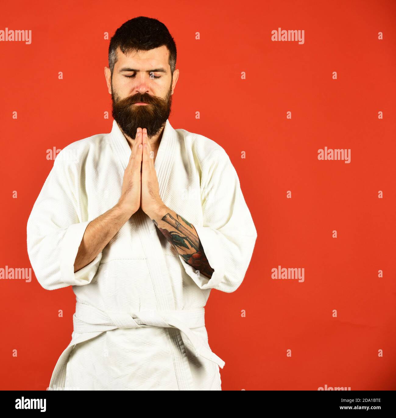 Man with beard in white kimono on red background. Combat master holds