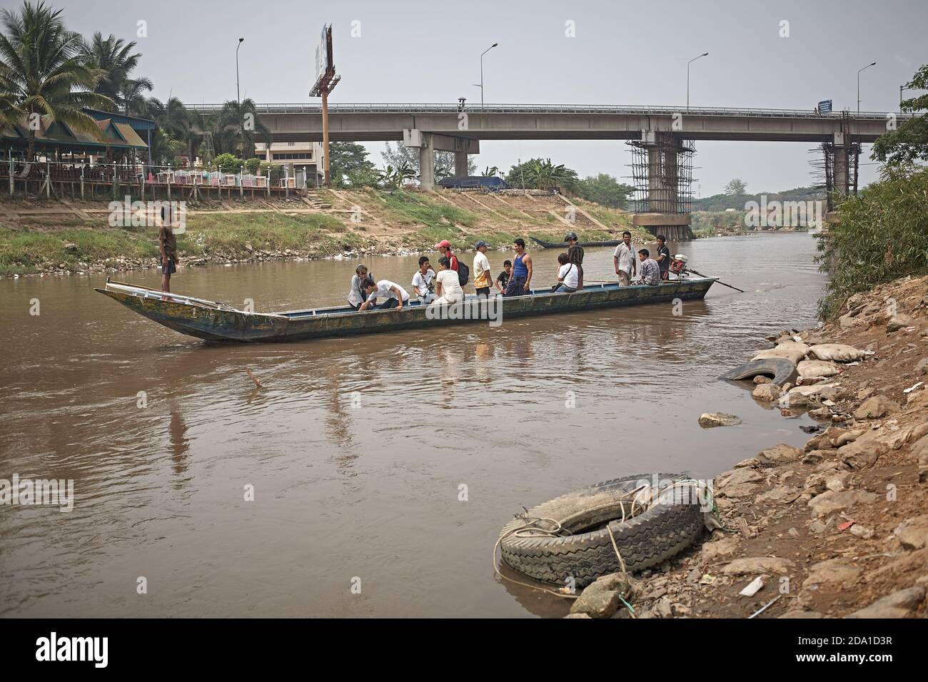 Mae Sot, Thailand. April 2012. Passenger boat crossing the river that serves as the border with Myanmar, with the bridge that joins the two countries Stock Photo