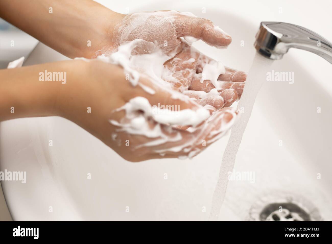 Child Washing of hands with soap with copious foam under running water in the bathroom over a white sink and chrome faucet. The concept of purity from Stock Photo