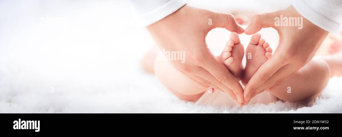 Mother Holding Baby's Feet In Heart Shaped Hands - Infant Care Concept Stock Photo