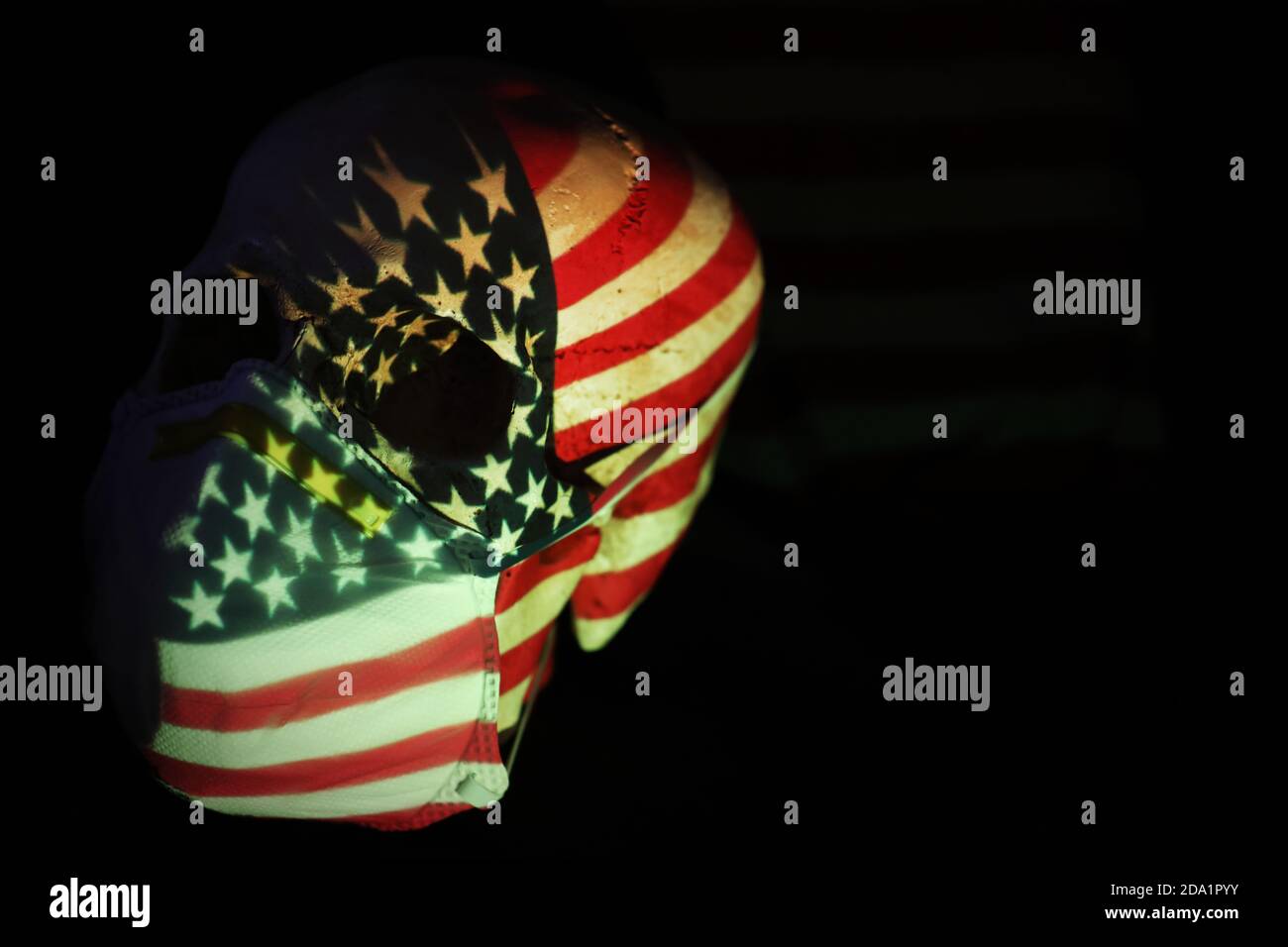 The American stars and stripes flag projected over a skull wearing a breathing face mask. Corona virus covid 19 global pandemic social distancing meas Stock Photo