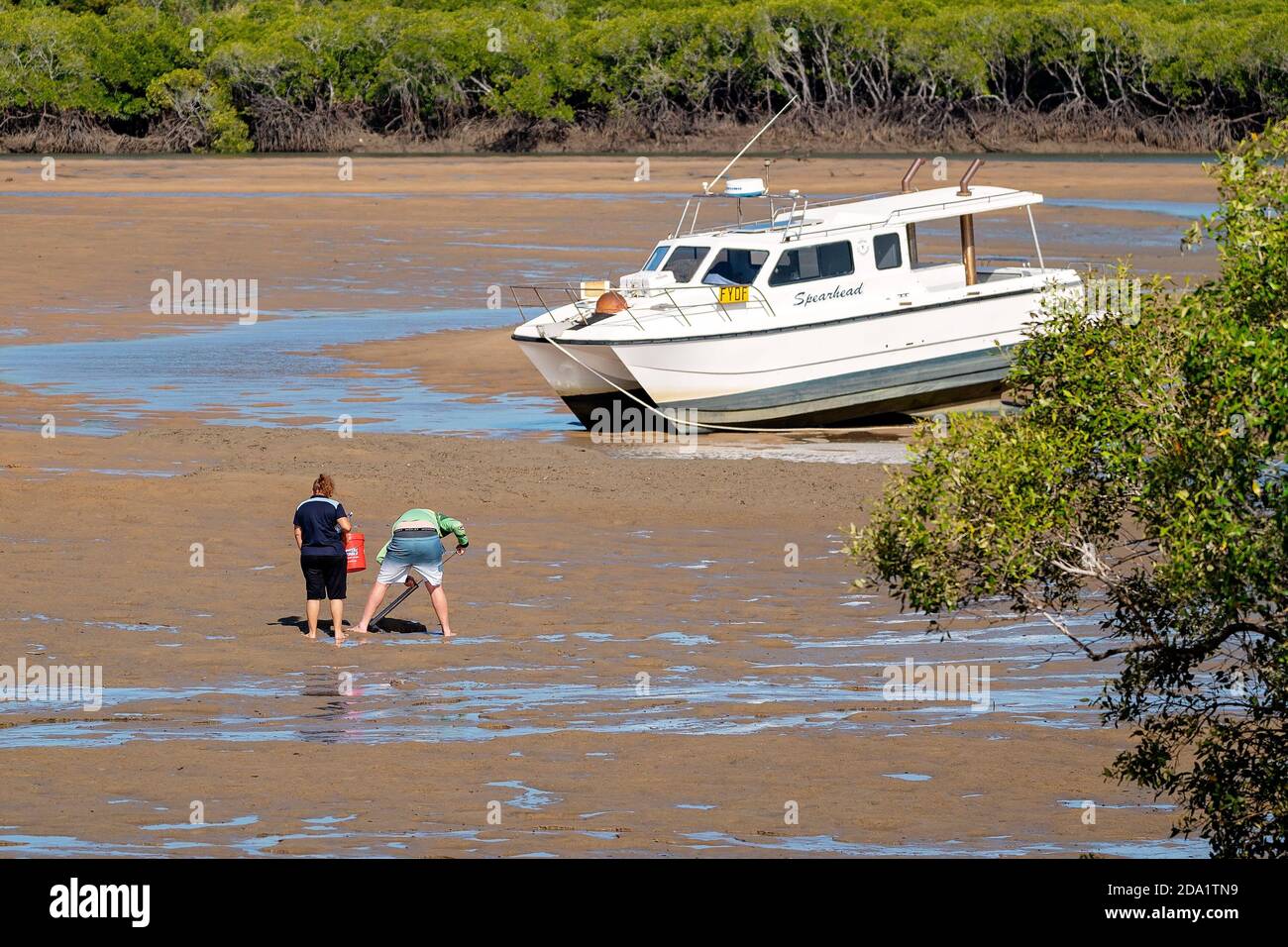 Mackay, Queensland, Australia - October 2019: A couple pumping for yabbies in the mud for bait to go fishing in front of a stranded boat Stock Photo