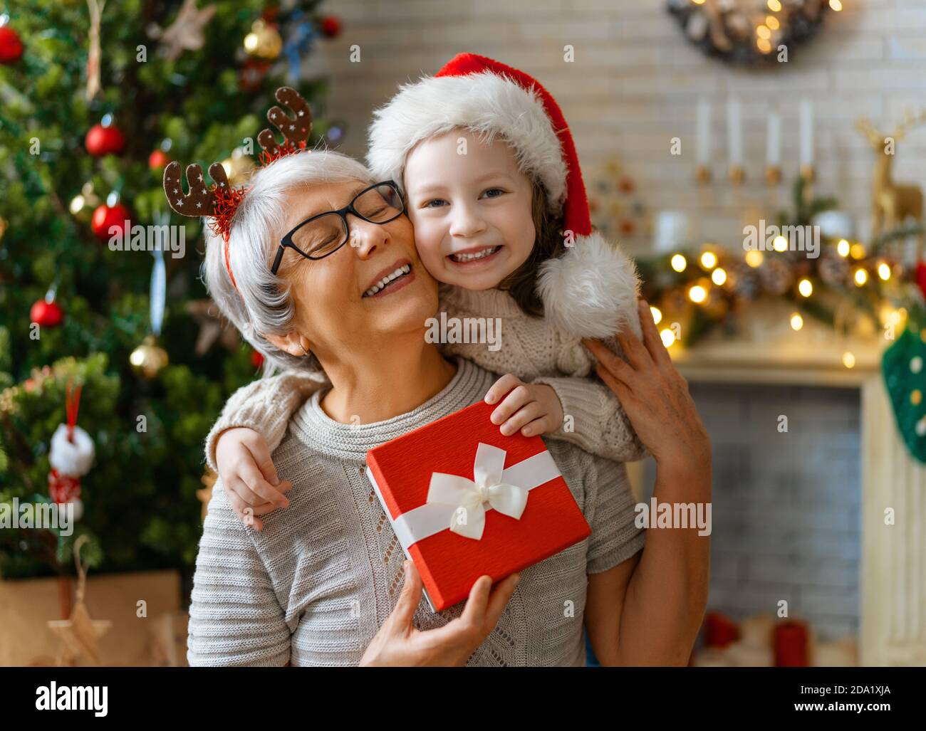 Premium Photo  Merry christmas and happy holidays! cheerful grandma and  her cute grand daughter girl exchanging gifts. granny and little child  having fun near tree indoors. loving family with presents in