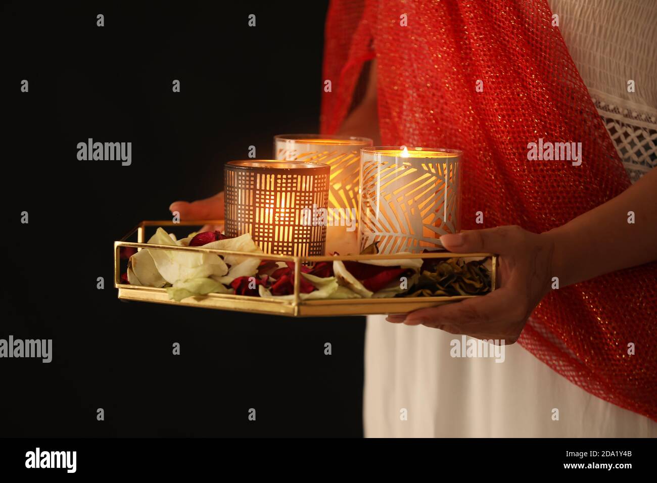 Woman holding tray with burning candles and flower petals for celebration of Divaly on dark background, closeup Stock Photo